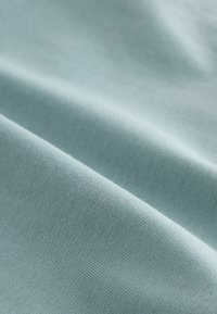 Helles blaues Baumwollgewebe mit einer glatten Textur, das feine Nähte und Falten zeigt und ein geschichtetes, drapiertes Aussehen erzeugt.