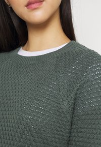Grüner gestrickter Pullover mit einem strukturierten, offenen Webmuster. Verfügt über einen Rundhalsausschnitt und einen leichten, atmungsaktiven Stoff.