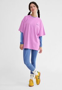 Overdimensioneret pink bomulds T-shirt med rund halsudskæring, lagdelt over en blå langærmet skjorte. Parret med blå ribbede leggings og multikolor sneakers.