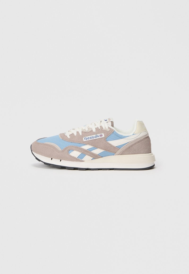 Reebok kedai, turintys šviesiai mėlyną tinklinį paviršių ir taupe zomšos viršutinę dalį, baltus odinius akcentus, apvalius raiščius ir struktūrizuotą gumos pado dizainą.