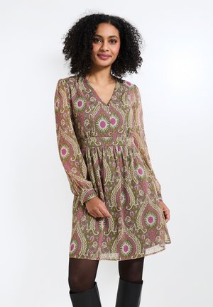 Vestido transparente de estampado floral en verde con acentos en rosa y blanco. Presenta mangas largas, escote en V y falda acampanada. Se lleva con botas negras.