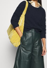 Granatowy dzianinowy sweter, zielone skórzane spodnie z szerokimi nogawkami oraz żółta teksturowana torebka z pionowymi plisami, noszona na ramieniu.