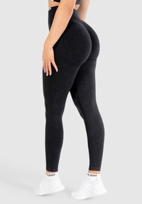 Leggings neri a vita alta con una finitura liscia e testurizzata e cuciture sagomate. Indossati con scarpe da ginnastica bianche e un top corto.