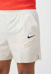 Shorts sportivi bianchi da uomo realizzati in tessuto leggero. Presentano spacchi sui lati e un logo Nike nero sulla tasca sinistra.