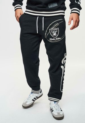 Zwarte sweatpants met een voetbalafbeelding en het "Raiders" logo. Voorzien van witte accenten, een verstelbare tailleband met koord en zijzakken.
