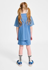 Haut de sport bleu et shorts avec une texture lisse, associés à des chaussettes à rayures en chevron noir et blanc et des chaussures bleues.