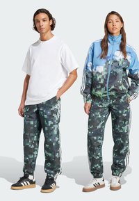Weißes oversized T-Shirt und blaue Camouflage-Jacke mit grünen Akzenten, kombiniert mit Camouflage-Hose. Beide Outfits verfügen über weiße Streifen an den Seiten.