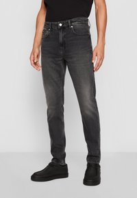 Černé slim-fit džíny s mírným pohodlným opotřebením, pět kapesním designem, lehkým poškozením a stříbrnými doplňky, spárované s černými botami.