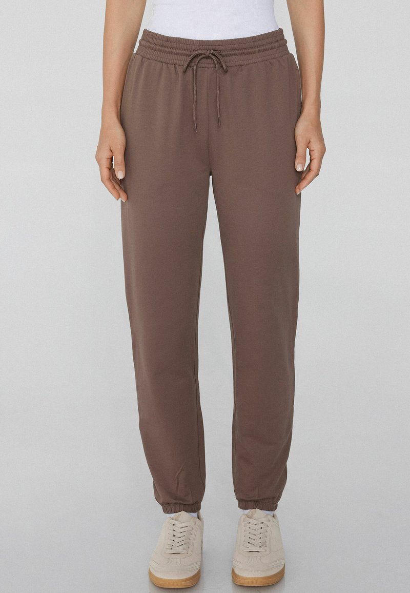 Braune Sweatpants aus weichem Stoff mit einem elastischen Taillenbund und Kordelzug, schmal zulaufenden Beinen und elastischen Bündchen.