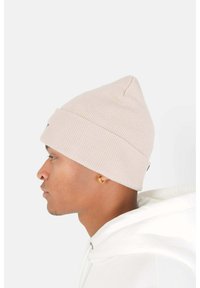 Berretto rosa a coste con la punta appuntita, con un piccolo logo tag sul lato. Indossato con una felpa bianca, mostrante il profilo laterale.