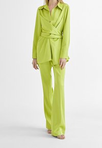 Limegrön skjorta med lång ärm och knytdesign, kombinerad med matchande vidbyxor. Slät textur med en subtil glans.