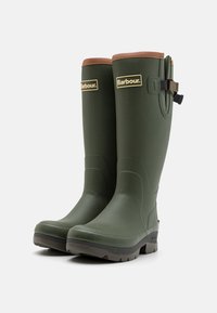 Groene rubberen laarzen tot de knie met een bruin leren rand en een verstelbare band. Voorzien van een gestructureerde afwerking en een duurzame rubberen zool.