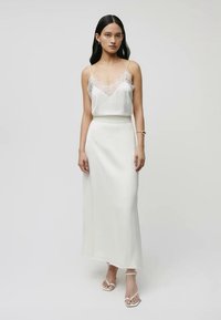 White satin dress with lace detailing on a V-neck top, fitted waist, and a straight, long skirt. Worn with strappy heels.