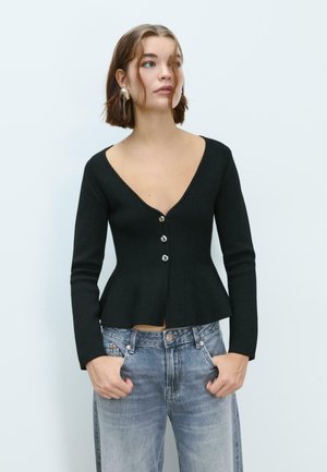 Crna pripijena cardigan jakna s dugim rukavima, V-izrezom i zatvaranjem na dugmad. Peplum dizajn u struku, upotpunjena svijetlim trapericama.