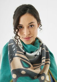 Écharpe en tricot présentant des motifs bleus, gris et beiges. Texture douce avec un design en spirale prononcé et des coutures accentuées contrastantes le long du bord.