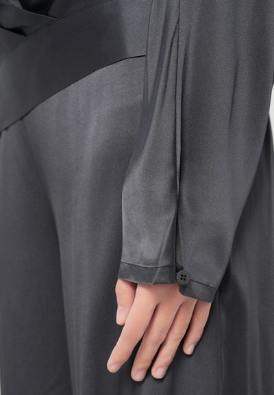 Îmbrăcăminte de culoare gri închis, cu textură mătăsoasă și netedă. Are o mânecă strâmtă, cu un detaliu de nasture negru unic la manșetă.