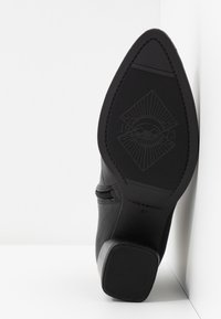 Semelle de botte noire à bout pointu avec motif texturé, talon bloc et taille 37 marquée, positionnée debout contre un coin blanc.