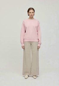 Hele roosa sweatshirt, millel on madalad õlavarred ja ribatud varrukad, koos laia heleda beeži pükstega. Jalatsiteks beežid libisemised.