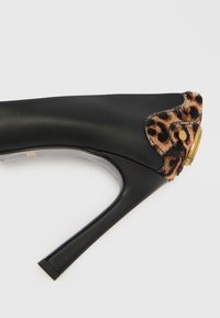Pantof cu toc înalt de culoare neagră, realizat din piele netedă. Prezintă un accent cu imprimeu de leopard și un detaliu cu buton auriu la toc. Formă de toc pătrat.