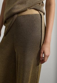 Pantalones de tela de punto a rayas doradas y negras con una textura suave, que presentan un detalle en la costura lateral. La cinturilla es elástica y ajustada.