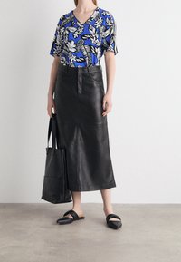 Blusa azul de manga corta con estampado floral, combinada con una falda de cuero negra de cintura alta. Las sandalias negras de tipo slider y un bolso tote completan el conjunto.