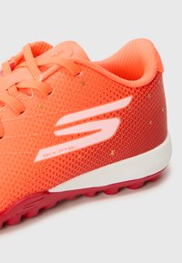 Adidași sport de culoare portocalie strălucitoare, având un superior din plasă texturată, accente roz, un logo alb și o talpă roșie cu crampoane proeminente pentru tracțiune.