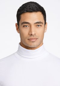 Camiseta de cuello alto blanca, hecha de un tejido suave, con un diseño ajustado, llevada por un modelo con cabello oscuro y corto.