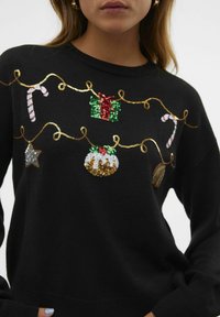Musthave mustar, millel on piduliku sädelusega kaunistused: kingitus, kommid, täht ja puding, paigutatud kuldse ahela kujundusele.