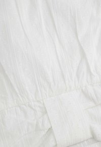 Biała tkanina z wypukłymi, teksturowanymi kropkami i pionowymi paskami. Elastyczny pas z podwiniętym akcentem. Lekki i gładki materiał.