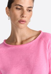 Felpa leggera in cotone rosa con scollatura ampia e dettagli a taglio vivo. Presenta una vestibilità rilassata e accenti a coste sulle maniche.