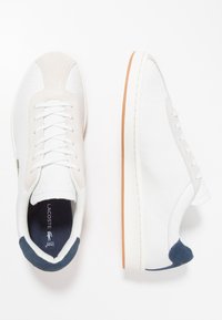 Baskets en cuir blanc avec un embout en daim beige, un dessus texturé, des lacets blancs et des accents de talon bleu marine. Semelle en caoutchouc avec un fond beige.