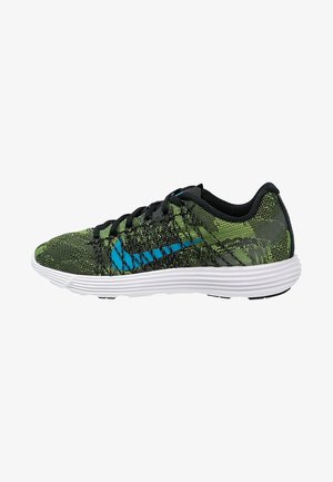 Chaussure de sport verte et noire à motif avec logo bleu, lacets noirs et semelle blanche amortissante, vue de côté sur fond blanc.