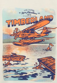 Illustratie van een watervliegtuig met oranje omtrekken dat over water vliegt, omringd door kano's, een pier en gestileerde golven. Tekst bevat "TIMBERLAND."
