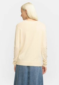Ljus beige långärmad tröja med rund halsringning, ribbade ärmslut och fåll, med en slät och mjuk textur.
