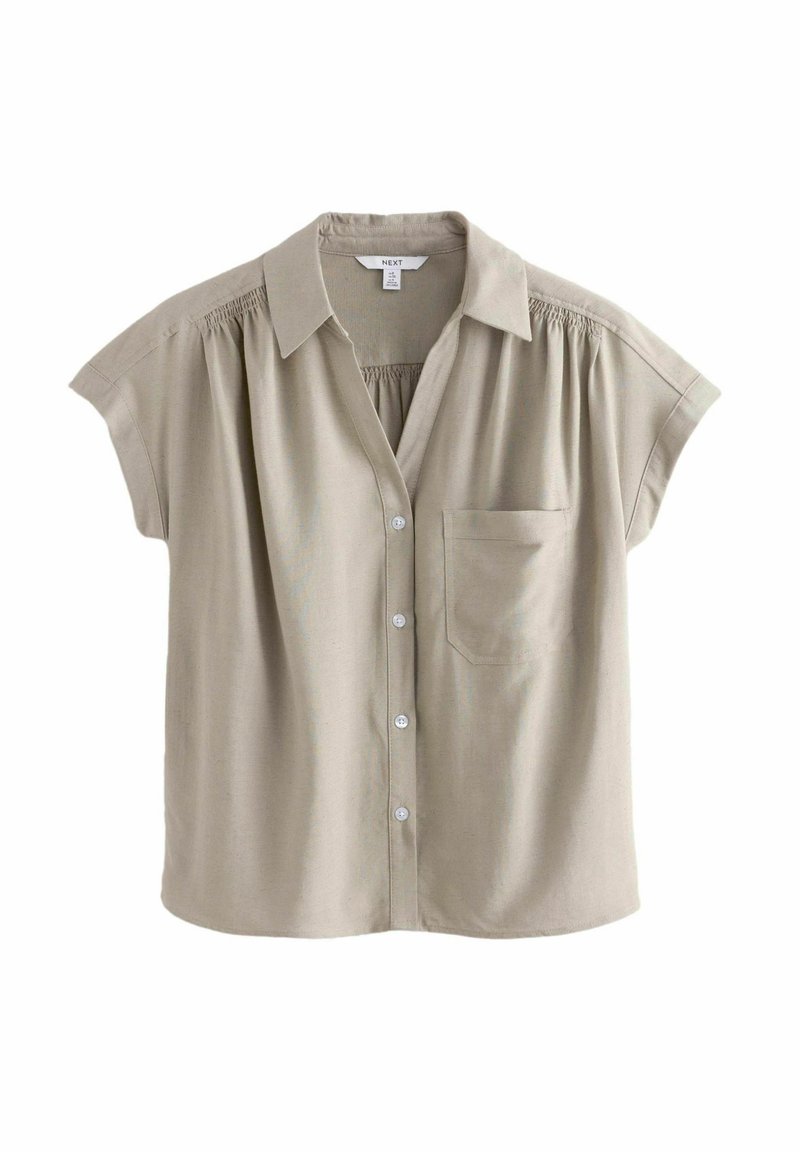 Korte mouwen, gekraagde blouse van lichtbeige stof met een knoopsluiting aan de voorkant, een zak aan de linkerkant en gesmokte details op de schouders.