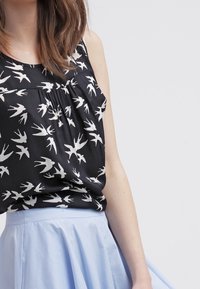 Top senza maniche nero con stampa di uccelli bianchi, con scollatura arricciata. Abbinato a una gonna azzurra chiara, che mostra un tessuto morbido e un design fluido.