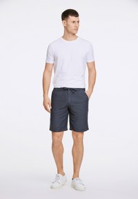 Herrars avslappnade outfit med en vit t-shirt med korta ärmar, marinblå shorts med dragsko och vita sneakers. Enkel, ren design.