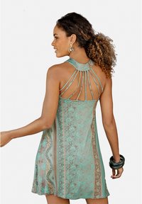 Akvac halter haljina s složenim cvjetnim uzorkom, dizajnom s izrezom na leđima i slojevitim naramenicama, koja se odlikuje lepršavim siluetom i teksturiranim materijalom.