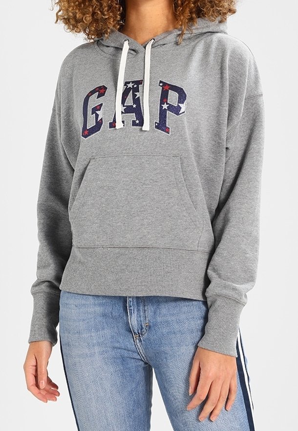 Felpa grigia con logo "GAP" in stelle rosse e blu, tasca a marsupio, cappuccio con cordino e polsini a costine. Indossata con jeans blu.