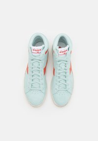 Des baskets montantes bleu clair avec des logos latéraux orange et des semelles blanches, vues de dessus sur un fond blanc uni.