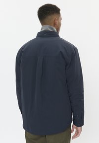 Chaqueta azul marino con un cuello gris, que cuenta con un pliegue en la espalda, mangas largas y puños abotonados. Hecha de una tela ligera.