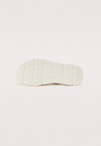 Hvit sneakersåle med teksturert gummi, med et rutenettmønster og merkelogo. Glatte og litt avrundede kanter ved tåen.