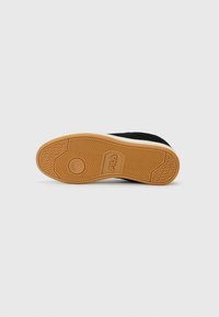 Suela de goma de una zapatilla FILA negra mostrando el patrón de la banda de rodadura y el logo de la marca, fotografiada desde abajo sobre un fondo blanco liso.