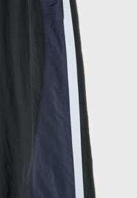 Sorte og marineblå stofpaneler med en lyseblå lodret stribedetalje, der viser et tæt billede af et tøjs sidesøm.