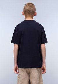 Camiseta de algodón azul marino con mangas cortas, cuello redondo y un corte relajado. La vista trasera muestra una textura suave sin logotipos ni diseños visibles.