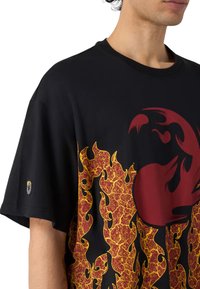 Sorte T-shirt med korte ærmer, der har et rødt og gult flamme-design. Blødt stof, rund halsudskæring og logo-detalje på ærmet.