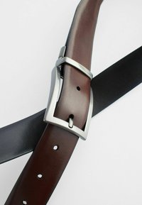 Brown and black leather belts intersecting, featuring a rectangular silver metal buckle and multiple holes for adjustment.