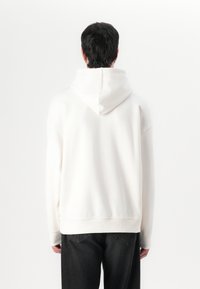 Weißer Hoodie mit großer Kapuze, lockerer Passform, gerippten Bündchen und Saum, kombiniert mit dunklen Jeans und einem glatten Stofftextur.