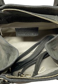 Interiér černé nubukové kabelky, s kapsou na zip, několika přihrádkami a štítkem s nápisem "Pravá kůže, vyrobeno v Itálii".