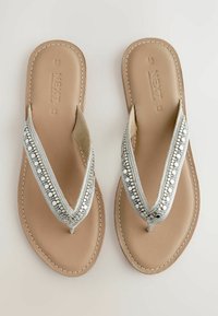Zilveren teenslippers met een decoratieve beaded band, vlakke leren binnenzool en gestikte details op de randen.